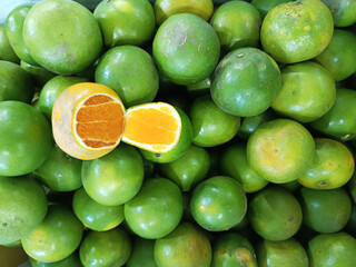 A pile of green tangerines with one cut open to reveal its bright orange interior, at a fresh fruit market.