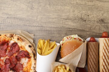 Different delicious fast food on wooden table, flat lay. Space for text