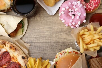 Frame of different delicious fast food and cola on wooden table, flat lay. Space for text