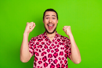 Fototapeta premium Excited young man expresses joy in vibrant style wearing pink leopard print shirt against green background