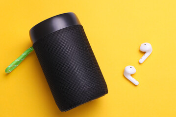 Wireless bluetooth stereo speaker with earphones on yellow background. Top view
