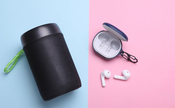 Wireless bluetooth stereo speaker with earphones on blue pink background. Top view