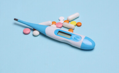 Modern electronic thermometer with tablets on a blue background. Diagnosis and treatment of colds and flu