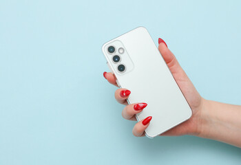 Female hand holding modern smartphone with three cameras on blue background