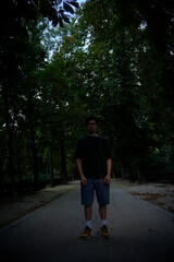 Obraz premium Young man standing on a path in a dark park at dusk