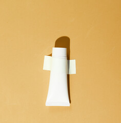 Cream tube is taped to yellow wall. Conceptual beauty photo, minimalism.