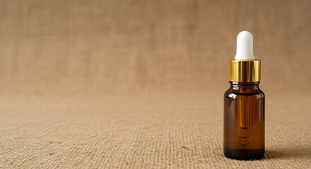 Naklejka premium Amber glass essential oil bottle with gold cap on textured neutral background