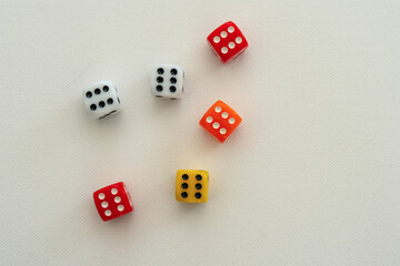 Dices in white, red, orange and yellow showing all the number six (6), on a white, textured canvas background.