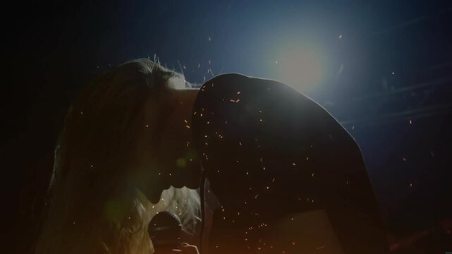 Singer raising head, lifting microphone under spotlight, scattering dust and belting note for music
