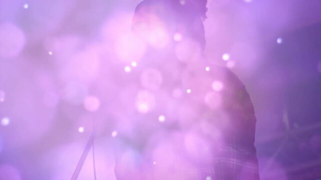 Singer pressing lips to mic and projecting voice on stage while violet haze swirling around