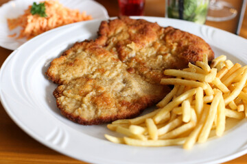 Delicious fried schnitzel with golden French fries on white plate. Traditional European lunch meal closeup. Crispy breaded meat cutlet served with side salad and refreshing drink background.