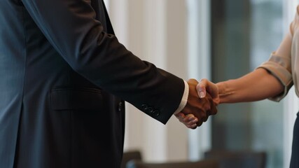 Businessman and Businesswoman shaking hands as a sign of partnership, teamwork or cooperation wearing business attire in a bright office background