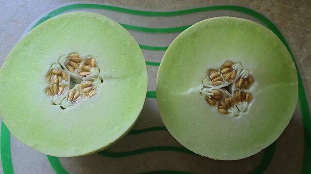 Slow zoom in of beautiful green melon honeydew fruit cut in half sitting on a cutting mat with kitchen background and lit by outdoors sunlight