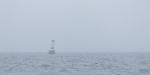 Marine channel marker on coastal rocks shrouded in fog. Moody Baltic Sea scene highlighting maritime safety, rocky shoreline, and mysterious northern coastal atmosphere