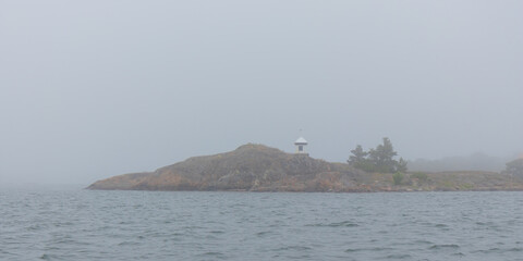 Marine channel marker on coastal rocks shrouded in fog. Moody Baltic Sea scene highlighting maritime safety, rocky shoreline, and mysterious northern coastal atmosphere
