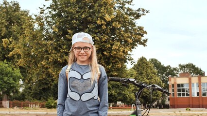 An 11 year old girl shows her thumbs up in a good mood next to her bicycle in the summer.