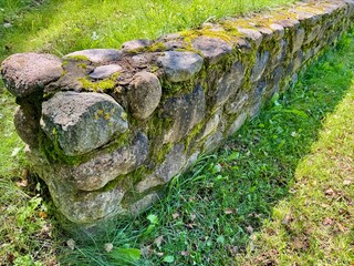  Rustic stone half wall covered with green moss in natural outdoor setting 