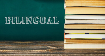 Stack of colorful books on wooden table with chalkboard background featuring bilingual text