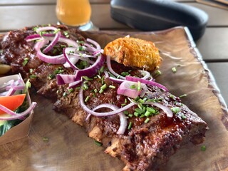 Delicious barbecue ribs with red onions and corn on the cob served on wooden board