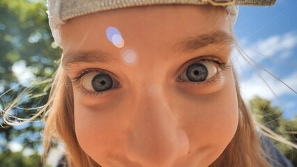 Schoolgirl wearing baseball cap, grinning with wide blue eyes, expressing playful childhood delight and lighthearted emotion