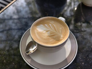 Latte art in a white cup with a spoon on a saucer perfect for coffee shops