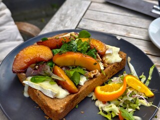 Gourmet toast with peaches brie walnuts and greens on a black plate for a delicious brunch