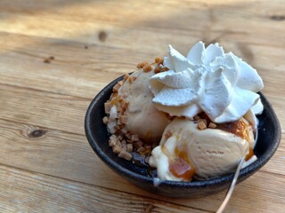 Delicious caramel ice cream sundae with whipped cream and toffee bits on a wooden table