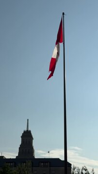 DOLLY SLOW MOTION SHOT - The Canadian flag waving in the breeze next to Toronto City Hall in Nathan Phillips Square, with the Canada Life Building in the background.
