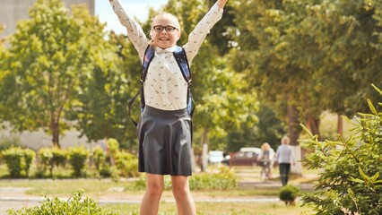Obraz premium Excited schoolgirl jumping with arms raised in celebration after school, enjoying freedom and happiness in a park