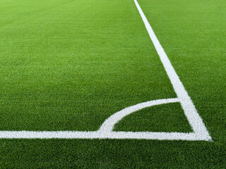 Fototapeta premium The football field corner with artificial green grass. Line in corner area of soccer field. Photo of a green synthetic grass sports field with white line shot from above. Football grass field corner.