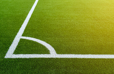 Fototapeta premium The football field corner with artificial green grass. Line in corner area of soccer field. Photo of a green synthetic grass sports field with white line shot from above. Football grass field corner.