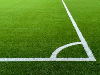 Obraz premium The football field corner with artificial green grass. Line in corner area of soccer field. Photo of a green synthetic grass sports field with white line shot from above. Football grass field corner.