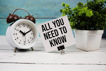 All You Need To Know text written on paper card with alarm clock on wooden background