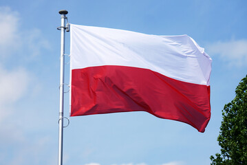 Polska flaga biało-czerwona powiewająca na maszcie na tle błękitnego nieba