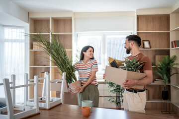 Happy couple carrying plants and boxes into new home