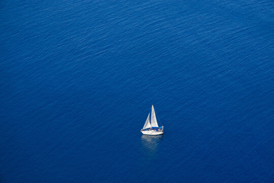 Yacht with white sails on a blue sea background. Top view.