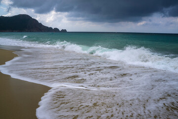 Waves crashing on sandy beach under cloudy sky