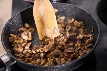 Mushrooms being in a skillet with a wooden spatula during dinner preparation in a cozy kitchen
