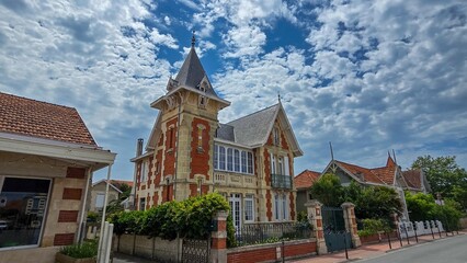 Naklejka premium One of charmante villas in the picturesque resort town Soulac-sur-Mer on the Atlantic, France. Against the background of a blue sky with white clouds.