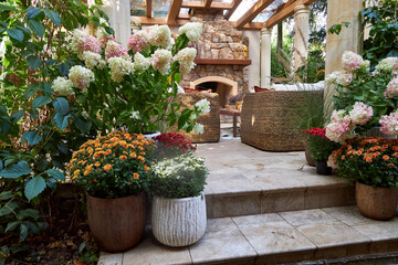 Cozy outdoor terrace with stone fireplace, wicker chairs, and colorful blooming flowers. A stylish garden patio blending rustic charm with natural elegance and relaxing atmosphere