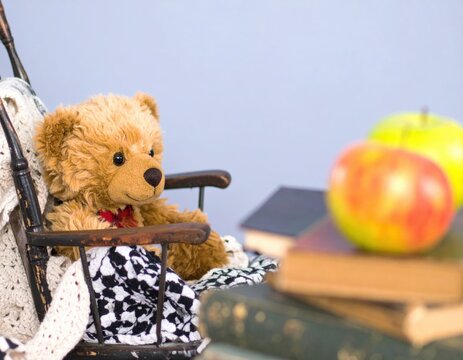 Teddy bear sitting in a rocking chair with apples and books