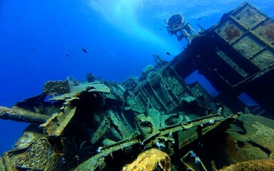 Part of sunken ship, the wreck structure  in the vivid blue ocean. Rusty metal parts and decks, underwater shipwreck in the sea and swimming fish. Travel photo, scuba diving, wreck exploration. 