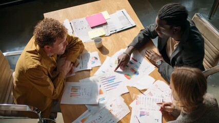 Diverse colleagues gathered around a table, reviewing data charts and graphs during a collaborative business meeting. - Powered by Adobe