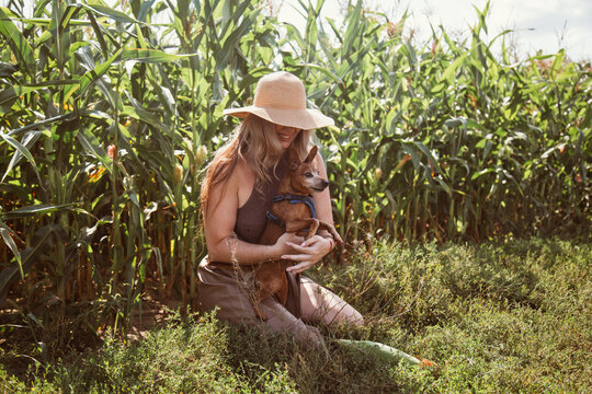 Woman gently holds her dog's head and leans in to kiss the dog s open mouth in a sunny grassy field under a bright sky, capturing a tender moment of affection
