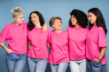 Five smiling women embracing and wearing pink shirts for breast cancer awareness