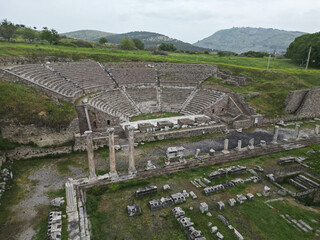 Ancient amphitheater and columns of Pergamon in Bergama Turkey The semi circular theater sits below a row of columns The area is filled with scattered stones and surrounded by lush green hills