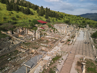 Hillside ruins frame the marble street of Ephesus in Turkey Travelers study columns and carved blocks The layout of homes and shops appears along the ancient road Historic stones line the way