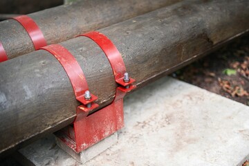 Metal pipes with concrete insulation and red brackets secured to a concrete base