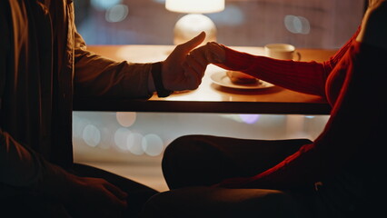 Tender couple holding hands at romantic night date in restaurant closeup. 