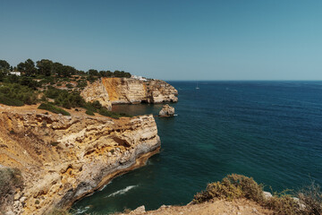 Algarve golden cliffs with rock formations, yacht, and coastal village in the distance, Portugal